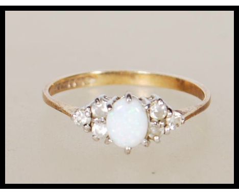 A hallmarked 9ct gold ring set with a opal cabochon flanked by six white accent stones. Hallmarked London 1989. Weight 1.0g. 