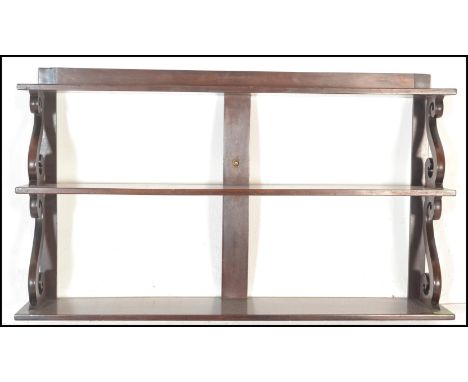 An early 20th Century mahogany graduating three tier wall hanging shelf rack having scroll side supports with a central strut