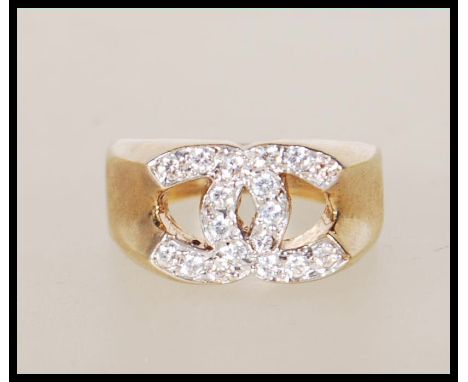 A stamped 9ct gold designer style ring with crossed C's to the head set with white accent stones. Weight 6.4g. Size O.5.