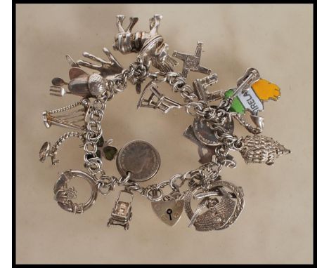 A silver heart lock charm bracelet having an assortment of charms to include hand, shire horse, crane, harp, pram, coins, hed