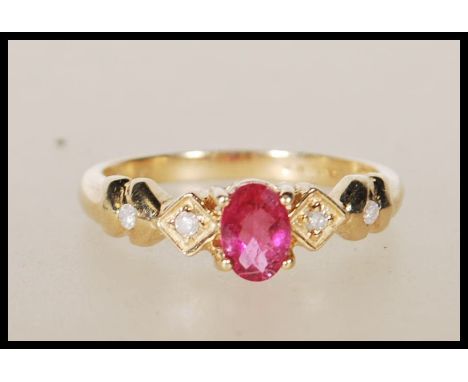 A hallmarked 9ct yellow gold ring having central oval faceted cut pink stone flanked by white accent stones on a decorative d