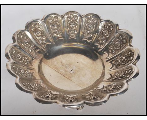 A stamped 800 silver dressing table trinket bowl having a scalloped rim with repousse floral decoration raised on three cab f