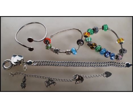 A selection of silver bracelets to include two snake chain bracelets having beaded charms, a cuff bangle having amber coloure