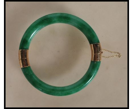 An oriental gold mounted green jade hinged bangle with two hinged sections of green jadeite united by a 14ct gold hinge and c