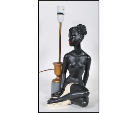 A vintage mid novelty 20th Century table lamp base in the form of a seated semi clad naked black lady being painted with red 