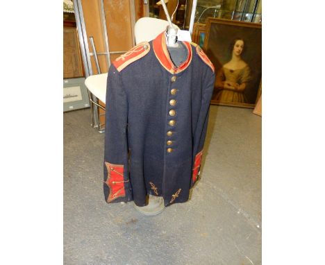 A VINTAGE BANDSMAN'S BLACK TUNIC WITH CRIMSON COLLAR AND CUFFS TOGETHER WITH A VINTAGE DISPLAY STAND.