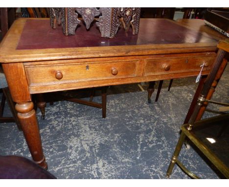 A RED LEATHER INSET OAK TWO DRAWER WRITING TABLE ON TURNED CYLINDRICAL LEGS TAPERING TO WHITE CERAMIC CASTORS.&nbsp; &nbsp;10