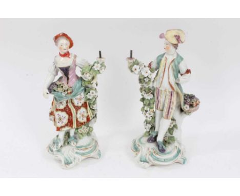 A pair of Derby figural candlesticks, late 18th century, each standing next to floral encrusted tree trunks, on scrollwork ba