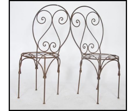 A pair of 20th century wrought iron garden chairs of strap work construction to the seats and arched back rests. 99cms x48cms