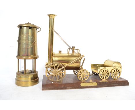 A vintage brass miners oil lamp together with a brass model of Stephensons Rocket on a plinth base with an applied brass plaq