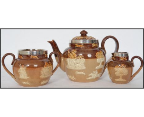 A Doulton Lambeth three piece stoneware harvest pattern tea service having silver rims being stamped to base. Hallmarked for 