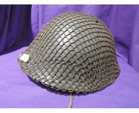 A metal military helmet covered in netting, very good condition