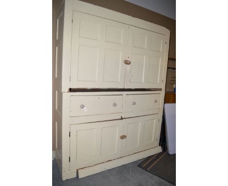 A large cream painted 19th Century cupboard with two panel doors enclosing shelves, above another similar piece of furniture 