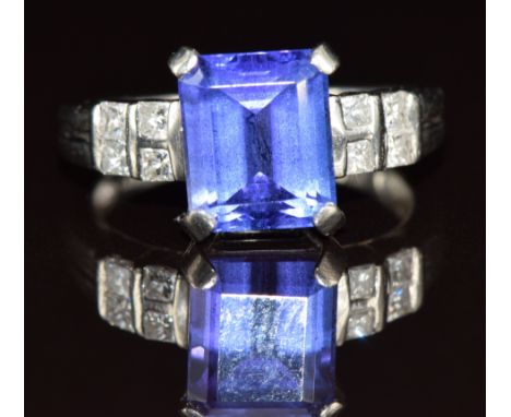 A platinum ring set with an emerald cut tanzanite of approximately 3.4ct and four princess cut diamonds to each shoulder, 6.1