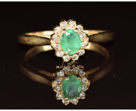 A 14k gold ring set with an oval cut emerald of approximately 0.4ct surrounded by diamonds, 2.6g, size N