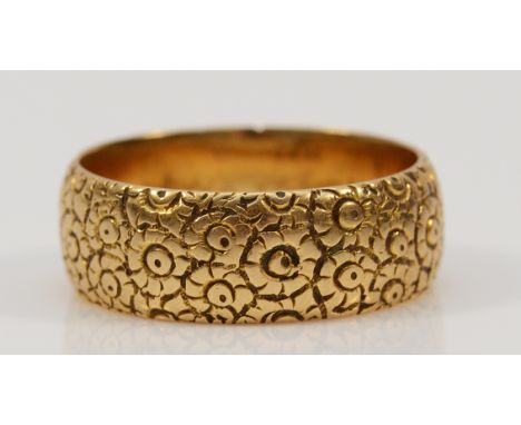 An 18ct gold floral patterned wedding band, 7mm wide, R, 8.5g Condition- This item is in overall good condition, no dents or 
