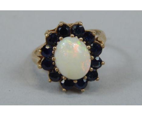 A ladies dress ring, florally set with central claw set opal, surrounded by small blue sapphire coloured stones, on a part pi