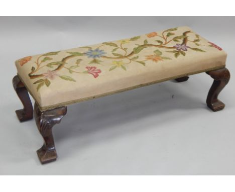 An early 20thC walnut fender type stool, with a crewelwork padded seat, on shell carved cabriole legs, with pointed pad feet,