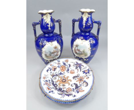 A pair of late 19thC Staffordshire pottery two handled vases, each painted with a country scene with cottages etc., on a blue