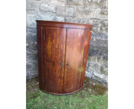 A 19th century oak bow fronted corner cupboard, the doors opening to reveal shelves, the two doors inlaid with shell motif, w