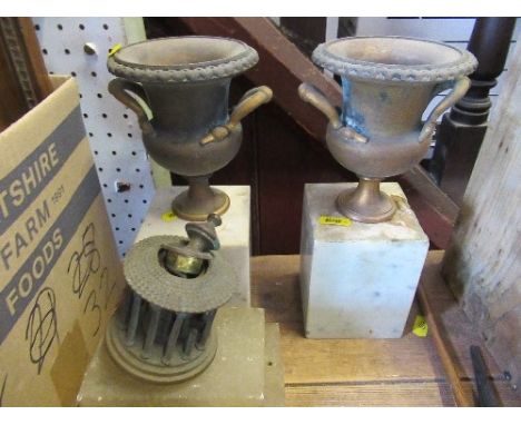 A pair of metal urns, on marble plinths, and another item