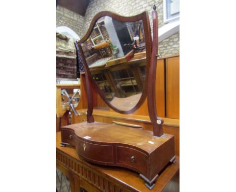 A 19th century mahogany shield shaped toilet mirror, raised on a platform/box base with serpentine front fitted with three fr