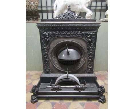 A large and decorative cast iron stove with raised trailing foliate, face mask, classical figures playing flutes and pipes, a