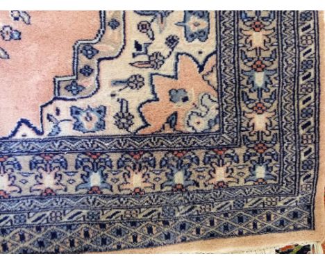 A pink ground wool carpet in the Persian style, the central medallion principally in a steel blue colourway, set within alter