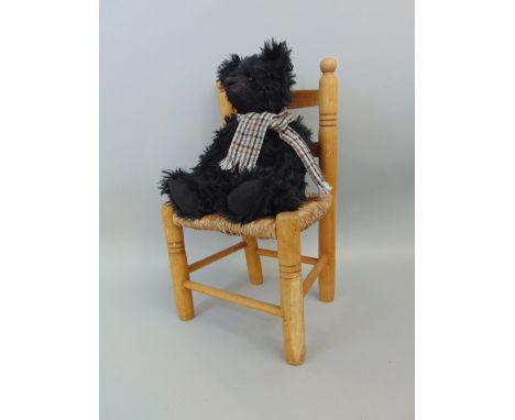 A vintage style black mohair teddy bear with tweed scarf and small beechwood and rush seated ladderback chair