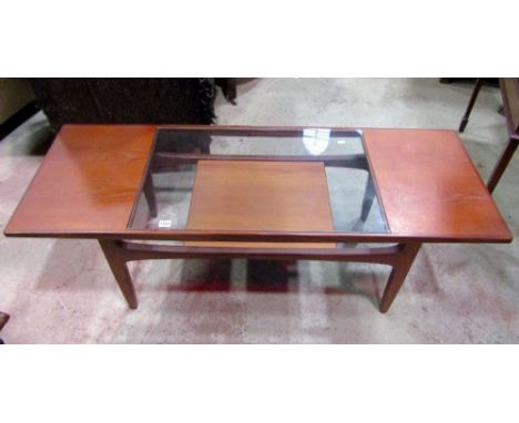 A 1970s teak coffee table of rectangular form with central inset glass panel, raised on four shaped supports united by a high