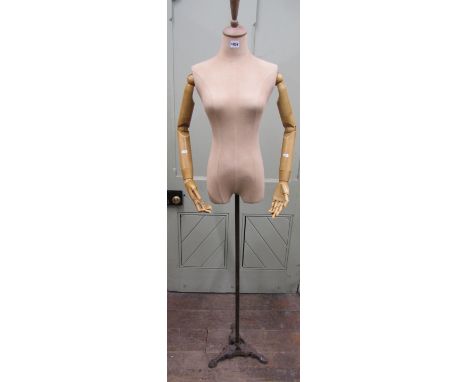 A female torso mannequin with fabric finish, the timber arms with articulated joints and fingers, raised on a steel column an
