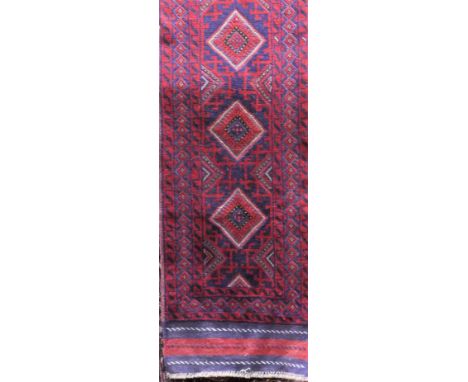 An eastern wool runner with repeating medallion centre, on an ink blue field within red geometric colourway, 250 x 60cm