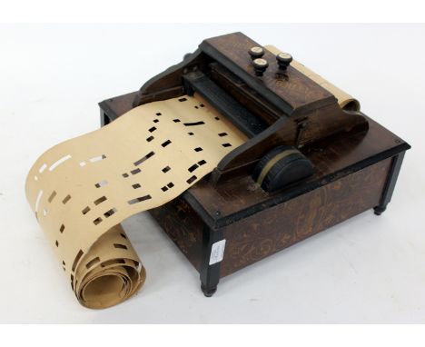 AN OLD WALNUT CASED ORGANETTE with applied scroll decoration playing rolls 19.6cm wide, complete with a quantity of further m
