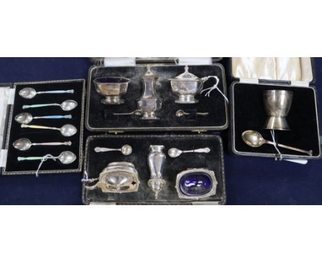 A set of six enamelled silver coffee spoons, an egg cup and spoon Christening set and two condiment sets, all cased