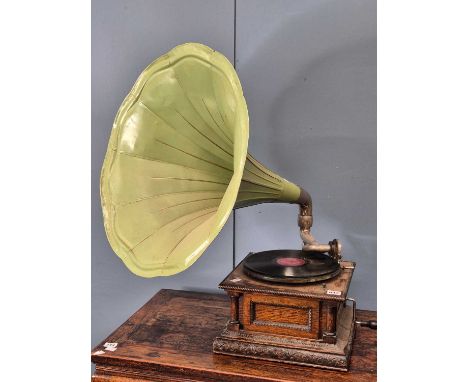 A vintage early 20th-century oak-cased table top gramophone with pale green flared metal horn. the base with carved decoratio