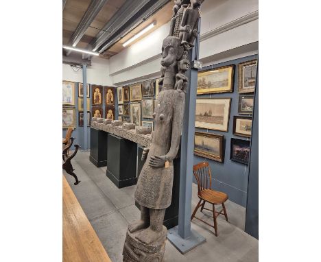 An Adu guardian post carved with a lady with two figures seated on her shoulders and two further above supporting the canoe c