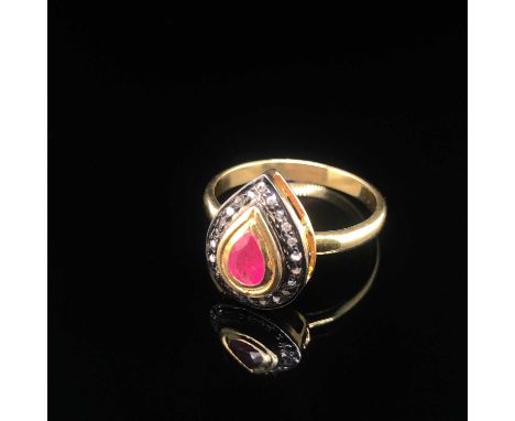 A pear-shaped ring set with a pear-shaped ruby and a halo or round brilliant cut diamonds set in unhallmarked silver gilt. Th