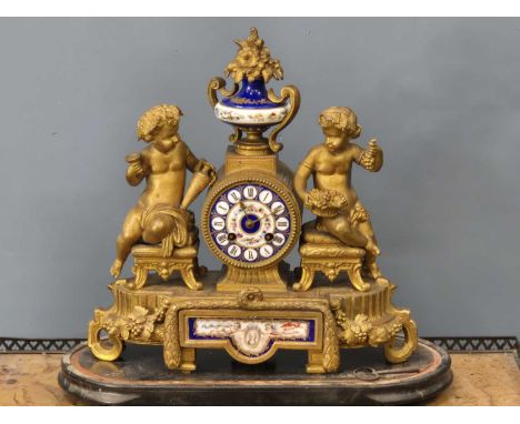 A Victorian gilt metal-cased mantle clock with a porcelain dial flanked by cherubic figures and surmounted with a porcelain u