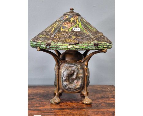 A Tiffany taste bronze lamp with leaded glass dragonfly shade supported on four arms around three lamp sockets and extending 