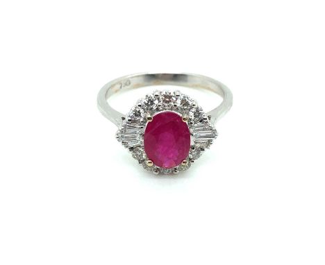 A ruby and diamond cluster ring. The central oval ruby is surrounded by a cluster of round brilliant and baguette-cut diamond