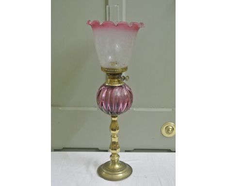 A vintage brass oil lamp with cranberry tinted melon shaped glass reservoir, knopped stem, circular stepped base, Duplex burn