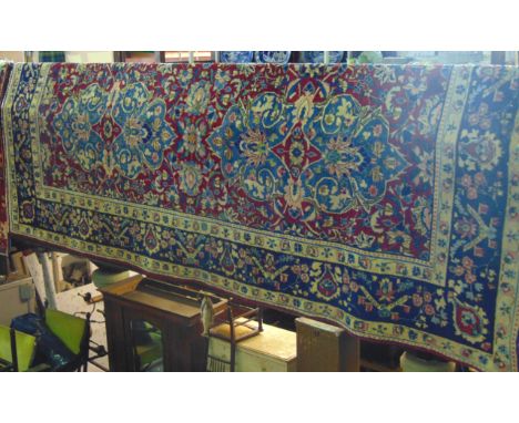 A substantial Persian style wool work carpet the central blue ground medallion upon a red field with abstract floral decorati