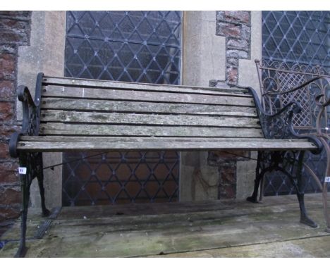 A weathered two to three seat garden bench with wooden slatted seat and combined back raised on a pair of decorative cast iro