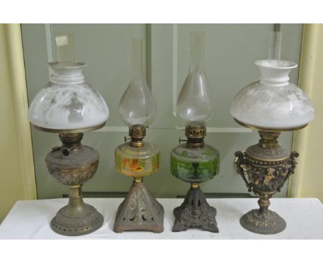 Four vintage oil lamps of varying design, two with coloured glass reservoirs and decorative cast iron bases, a further in cas