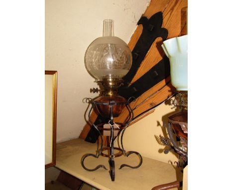An Arts and Crafts style oil lamp the organic scrolled ironwork frame united by graduated copper rings beneath a drop in copp