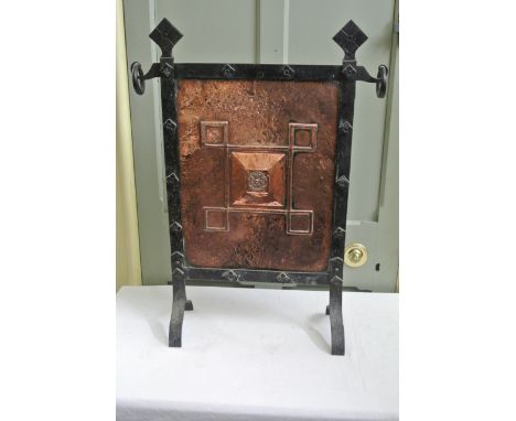 An Arts and Crafts fire screen the cast iron frame enclosing a copper beaten panel with geometric detail.