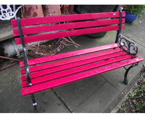 A small two seat garden bench with painted wooden slatted seat and back rails raised on a pair of decorative cast iron end su