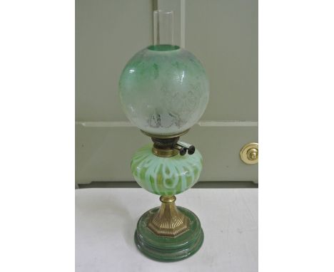 A Victorian oil lamp with Eureka brass burner, two tone mottled Vaseline glass reservoir, brass stem, green glazed circular m