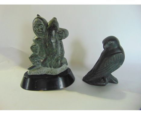 An Inuit type carved stone study of a figure in a parka coat lifting a seal upon his shoulder, signed indistinctly to undersi