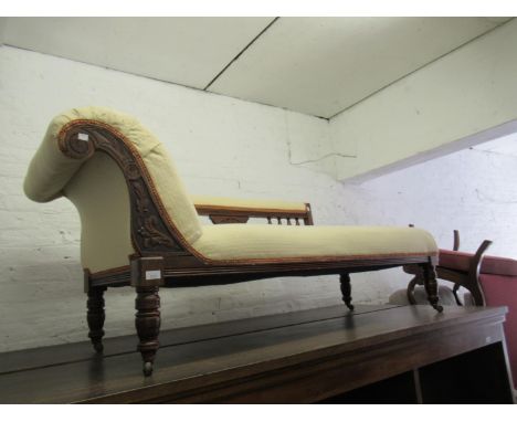Late 19th Century carved oak chaise longue having spindle back and cream upholstery, raised on turned tapering supports with 